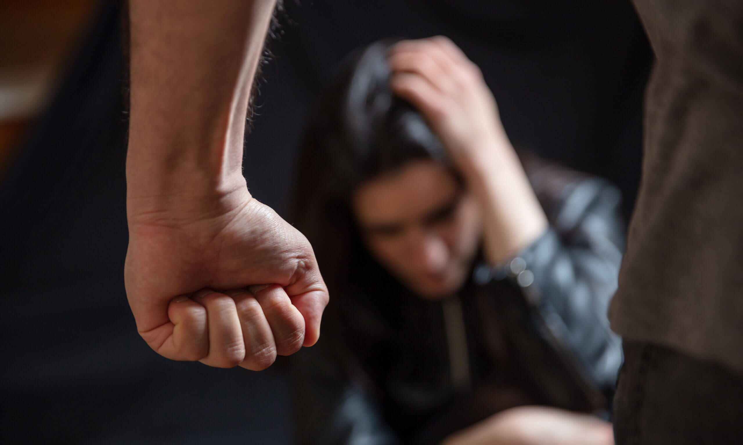 Woman abuse, Young woman scared holding head with hands, male clenched fist close up. Domestic violence, husband against wife. Dark room background