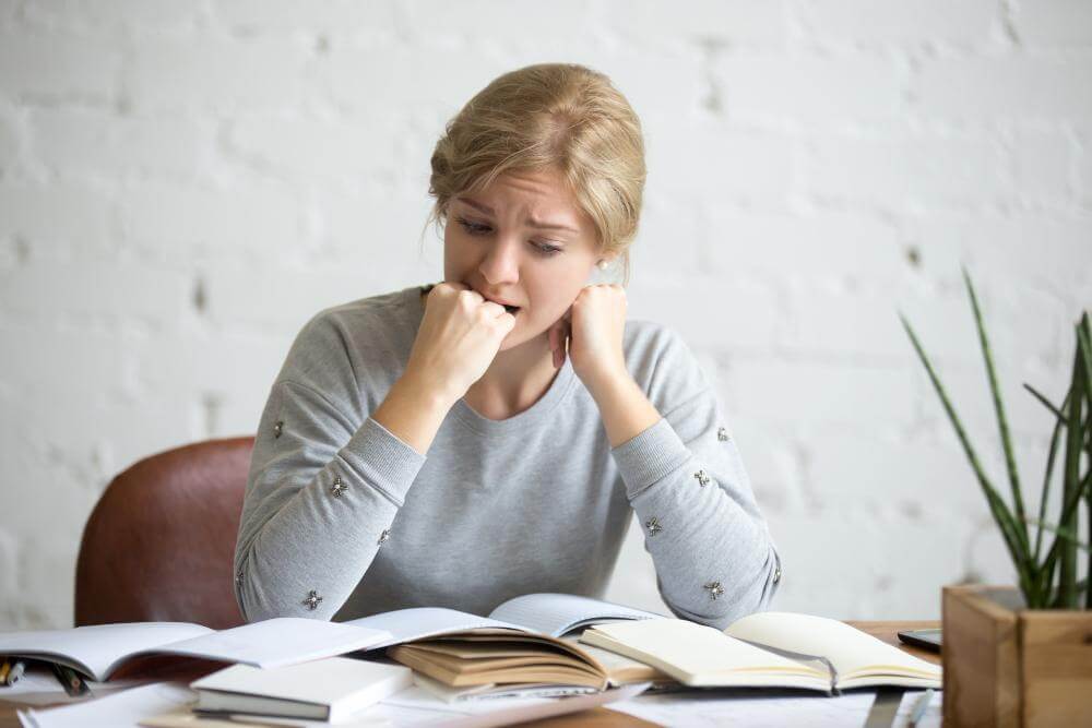 portrait-student-girl-sitting-desk-biting-her-fist